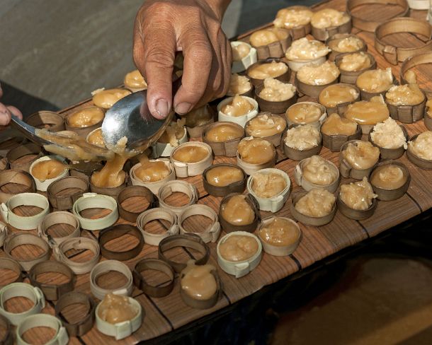 sm_khN1200 Caramelized palm sugar being filled into small palm leaf molds to procuce palm sugar sweets, Siem Reap, Cambodia