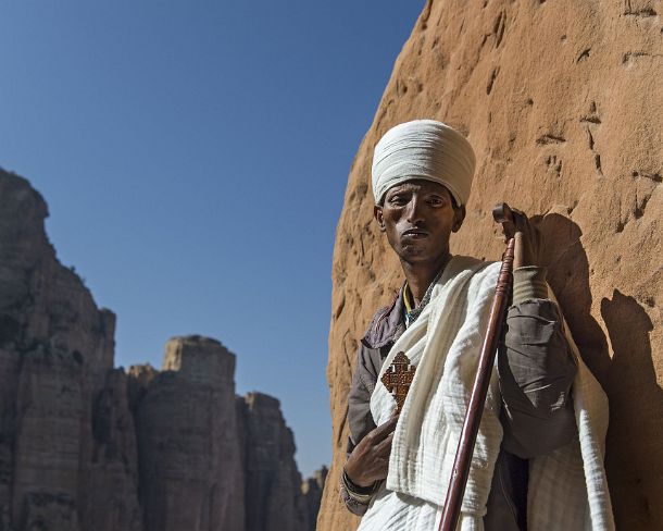 sm1gva_ET_cx2479_g Coptic priest standing at the entry to the rock-hewn church Abuna Yemata situated high up at a steep rock pinnacle, Gheralta, Tigray, Ethiopia