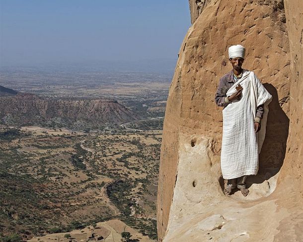 sm1gva_ET_cx2504_g Coptic priest standing at the entry to the rock-hewn church Abuna Yemata situated high up at a steep rock pinnacle, Gheralta, Tigray, Ethiopia