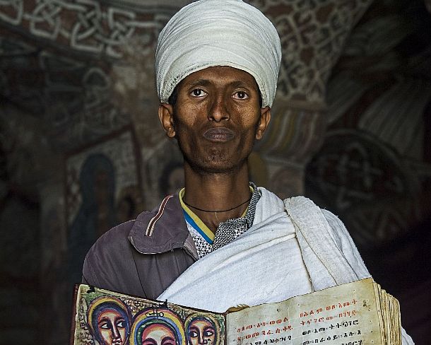 smgva_ET_x2482_g Orthodox priest of rock-hewn church Abuna Yemata showing a book of the miracles of Maria hand-written in Ge'ez language on parchment, Gheralta, Tigray, Ethiopia